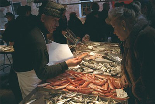 A fishmonger and a customer interacting across a counter covered with bins of fish in Venice's Rialto Markets. A fishmonger and a customer interacting across a counter covered with bins of fish in Venice's Rialto Markets.