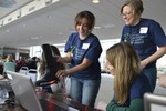 Three women are by a computer, holding a boot with wires attached to the computer.